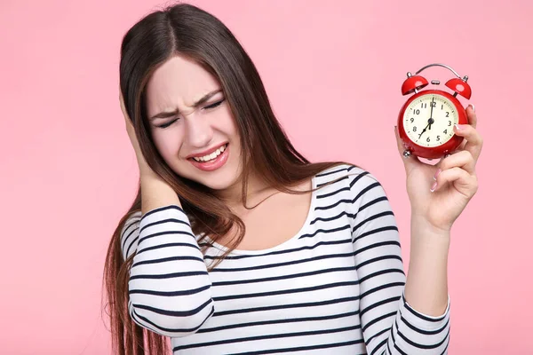 Bella giovane donna con sveglia rossa su sfondo rosa — Foto Stock