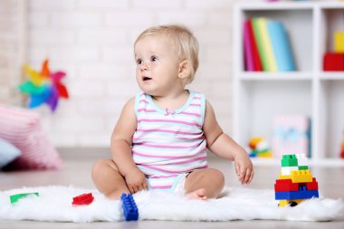 Oyuncaklar ile beyaz halı üzerinde oturan bebek kız