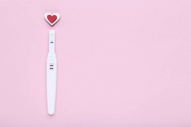 Pembe arka planda kırmızı kalpli gebelik testi