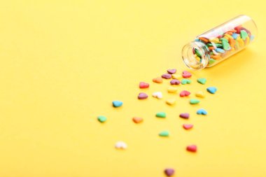 Sarı arka plan üzerinde cam şişe renkli kalp şeklinde sprinkles
