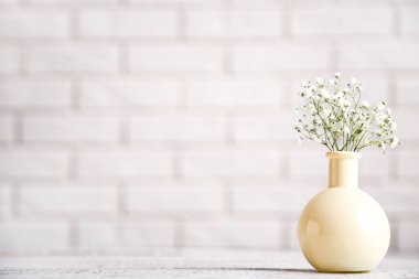 White gypsophila flowers in vase on brick wall background