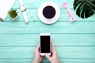 Ahşap masa üzerinde kahve, kol saati ve gözlük fincan ile kadın elinde Akıllı telefon