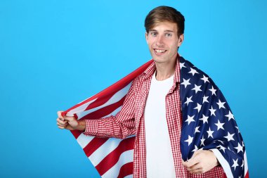 Bir Amerikan bayrağı mavi arka plan üzerinde tutan güzel genç adam