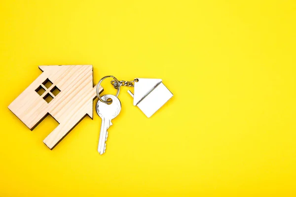 Silver key with wooden house on yellow background