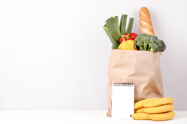 Grocery shopping bag with food and blank notepad on grey background