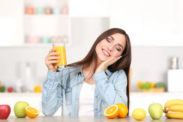 Piękna kobieta z kieliszek soku pomarańczowego i owoców siedzących w — Zdjęcie stockowe