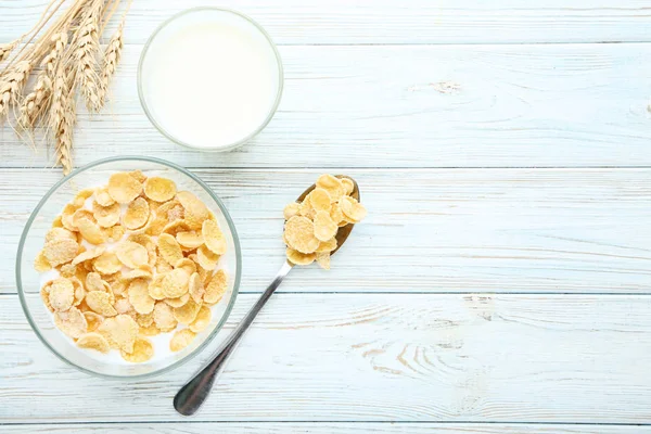 Corn flakes in milk with wheat ears on wooden table