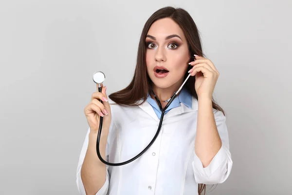 Retrato de jovem médico com estetoscópio sobre fundo cinza — Fotografia de Stock