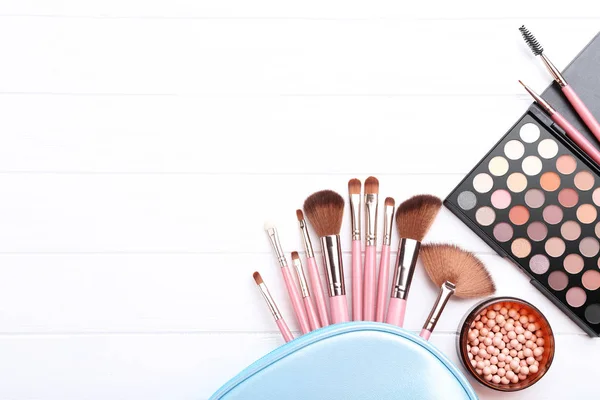 Makeup brushes with palette on white wooden table