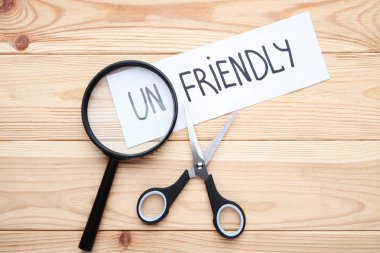 Kağıt kelime Unfriendly, makas ve ahşap masa üzerinde büyüteç ile