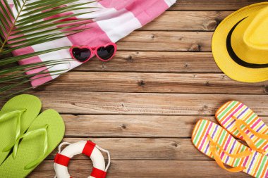 Kahverengi ahşap masa üzerinde şapka, havlu ve palmiye yaprağı ile renkli parmak arası terlik çiftleri