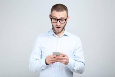 Gri arka planda akıllı telefonu olan gözlüklü genç adam.