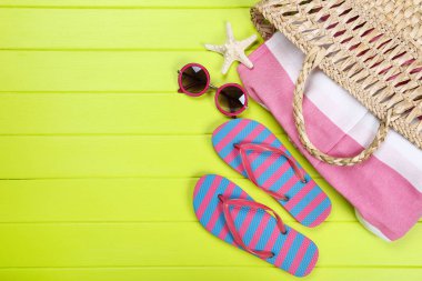 Yeşil ahşap masa üzerinde denizyıldızı, güneş gözlüğü ve çanta ile parmak arası terlik çifti