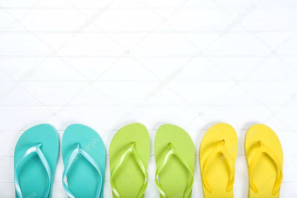 Pairs of colorful flip flops on white wooden table