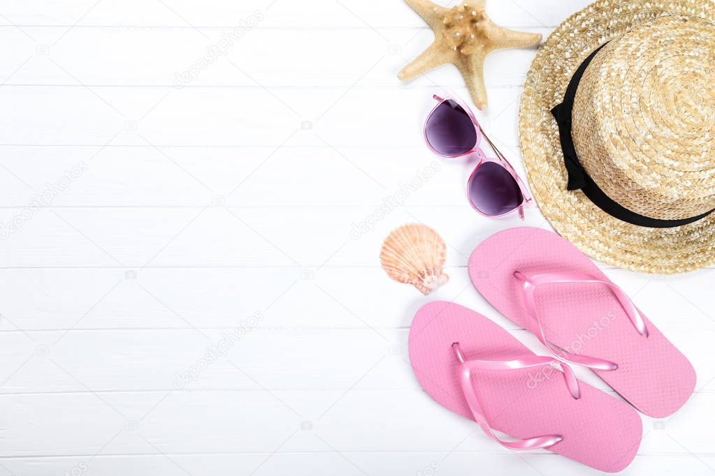 Pair of flip flops with seashells, hat and sunglasses on white wooden table