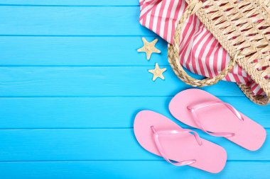 Mavi ahşap masa üzerinde denizyıldızları ve çanta ile parmak arası terlik çifti