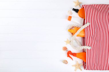 Beyaz ahşap üzerinde deniz kabukları ve çizgili çanta ile güneş kremi şişeleri