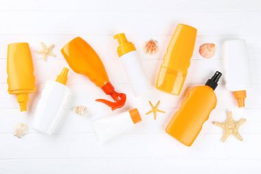Beyaz ahşap masa üzerinde deniz kabukları ile güneş kremi şişeleri