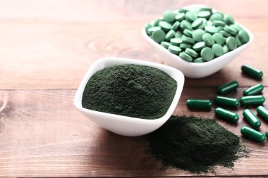 Spirulina tozu ve tabletler kahverengi ahşap masa üzerinde kaselerde