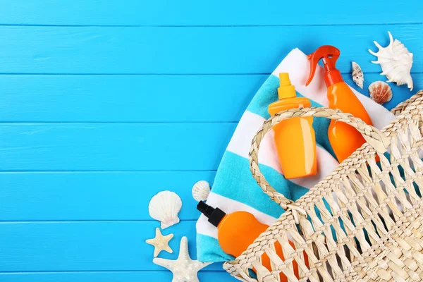 Αντιηλιακά μπουκάλια με κοχύλια, τσάντα και πετσέτες σε μπλε ξύλινο — Φωτογραφία Αρχείου