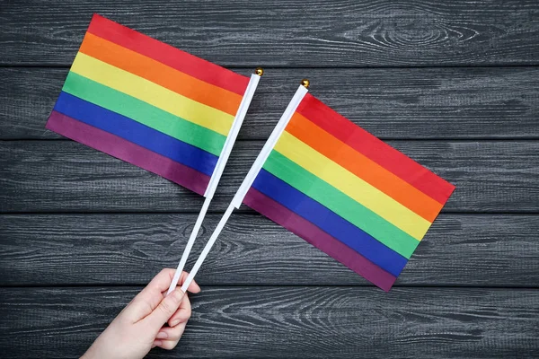Vrouwelijke hand houden Rainbow vlaggen op zwarte houten tafel — Stockfoto