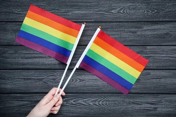 Mano femenina sosteniendo banderas de arco iris en mesa de madera negra — Foto de Stock