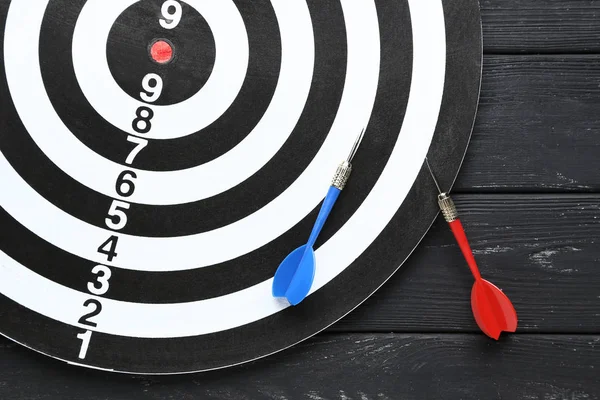 Dartboard com dardos na mesa de madeira preta — Fotografia de Stock