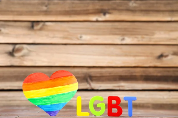 Abbreviation LGBT with rainbow heart on brown wooden table