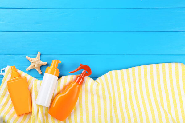 Sunscreen bottles with starfish and towel on blue wooden table