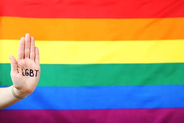 虹の旗の背景にLgbtの略語を持つ女性の手のひら — ストック写真