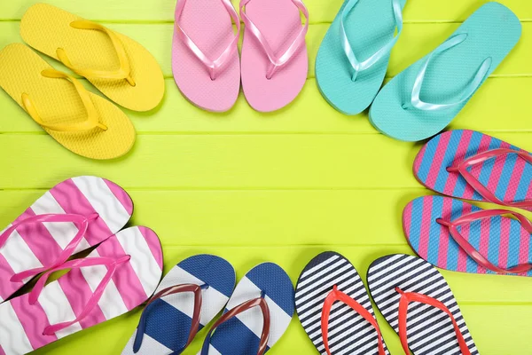 Pairs of colorful flip flops on green wooden table — Stock Photo, Image