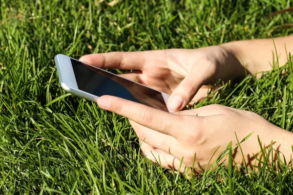 Woman holding and using smartphone on green grass