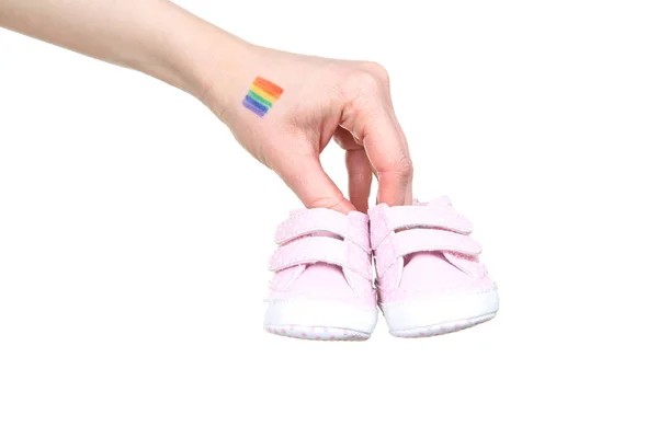 Vrouwelijke hand met tekening regenboog vlag en baby slofjes op wit ba — Stockfoto
