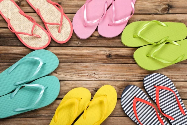 Pairs of colorful flip flops on brown wooden table — Stock Photo, Image