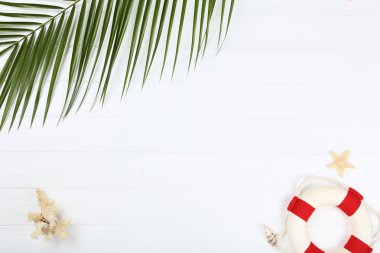 Whtie ahşap masa üzerinde lifebuoy ve palmiye yaprağı ile deniz kabukları