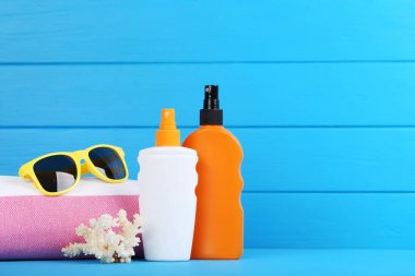 Mavi ahşap üzerinde mercan, havlu ve güneş gözlüğü ile güneş kremi şişeleri