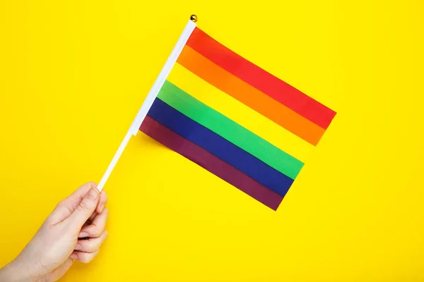 Mano femenina sosteniendo bandera del arco iris sobre fondo amarillo — Foto de Stock