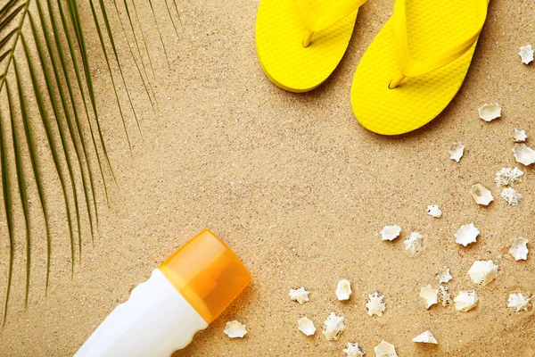Chinelos com concha e creme hidratante na areia da praia — Fotografia de Stock