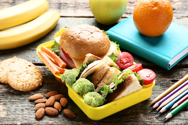 School lunch box with sandwich and vegetables on wooden table