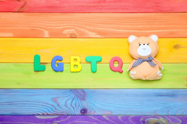 Abbreviation LGBT with soft bear toy on colorful wooden table