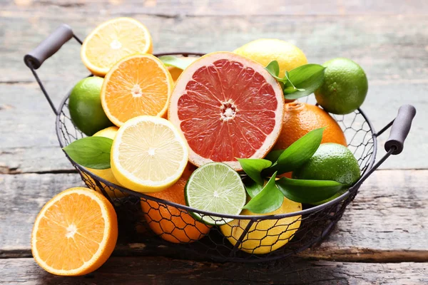 Citrusvruchten met groene blaadjes in mand op grijze houten tafel — Stockfoto