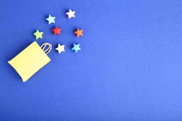 Étoiles en papier coloré avec sac à provisions sur fond bleu — Photo
