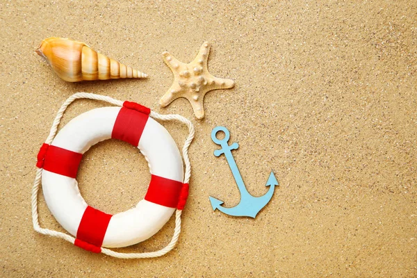 Seashells with lifebuoy and blue anchor on beach sand — Stock Photo, Image