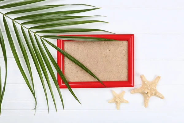 Wooden blank frame with starfishes and palm leaf on white table — ストック写真