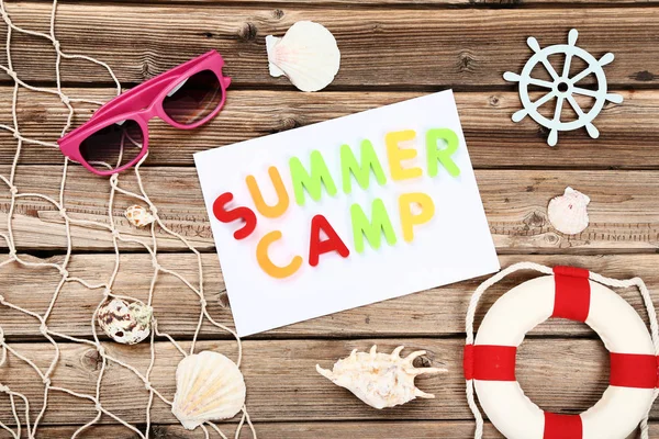 Texto Campamento de verano con conchas marinas, gafas de sol y boya salvavidas en la frente — Foto de Stock