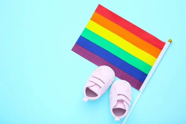 Rainbow flag with baby shoes on blue background — Stock Photo, Image