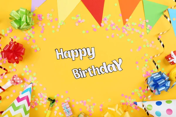 Texto Feliz Aniversário com decorações de festa em fundo amarelo — Fotografia de Stock