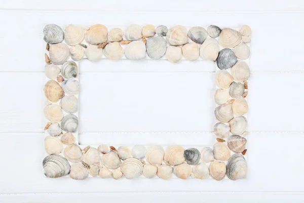 Wooden blank frame with seashells on white table — ストック写真