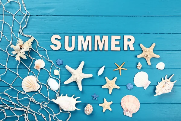 Palabra de verano con conchas marinas y red de pesca en mesa de madera azul —  Fotos de Stock