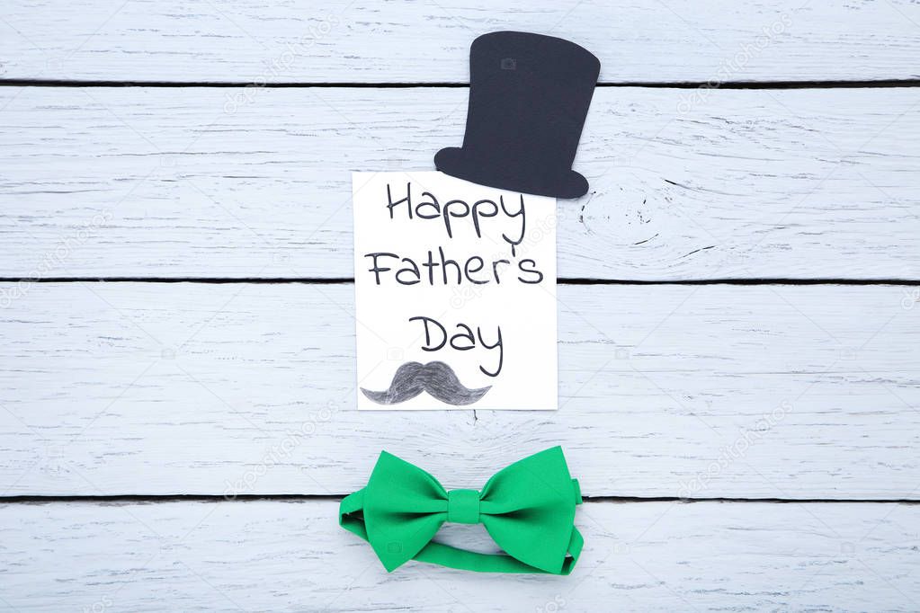 Text Happy Fathers Day with paper hat and bow tie on wooden tabl